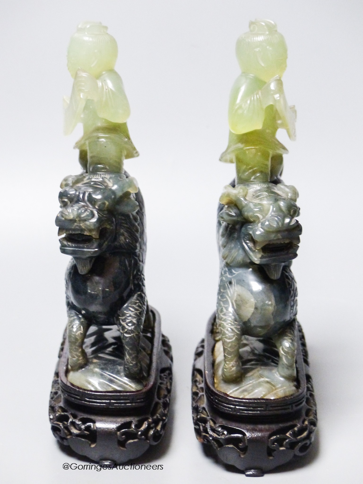 A pair of Chinese bowenite Jade figures of boys riding a qilin, mid 20th century, wood stands